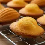 Freshly baked madeleine cookies recipe using cream, golden brown and cooling on a wire rack.